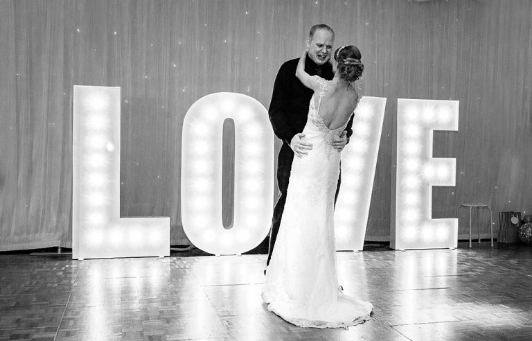 stylish photo of wedding couple first dance with love sign in background